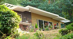 عکس از خانه ای با سقف مسطح که در یک دامنه و در یک مکان جنگلی مرتفع شده است