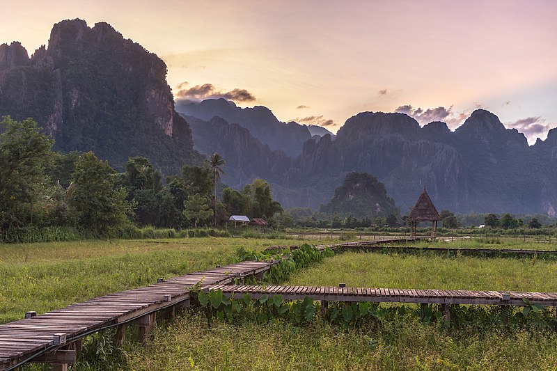 File:Wooden walkway leading to a hut with straw roof in front of karst mountains at sunset, Vang Vieng, Laos.jpg