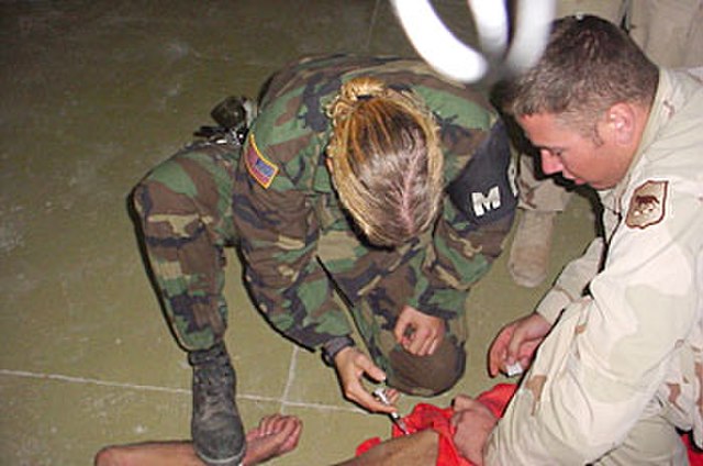 US Military Police officer restraining and sedating a prisoner, while a soldier holds him down