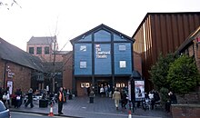 Entrance through the old The Other Place (blue building). The theatre (stage, back-stage and auditorium) was in the brown corrugated box to the right. Courtyard Theatre Stratford upon Avon.jpg