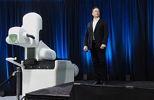 Musk standing next to bulky medical equipment on a stage
