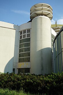 A cylindrical pylon at the entrance to the Queens Theatre, formerly the Theaterama. A tiered metal lantern is placed atop the pylon.