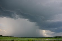 Black storm clouds under which a grey sheet of rain is falling on grasslands.