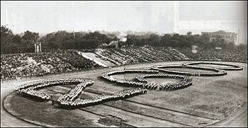 Fotografía en blanco y negro de grupos de individuos que forman el número 2600 en el césped central de un estadio.