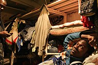 A refugee man sleeps on a shelf Ivorian refugees sleeping on shelves, Tel Aviv 2008.jpg