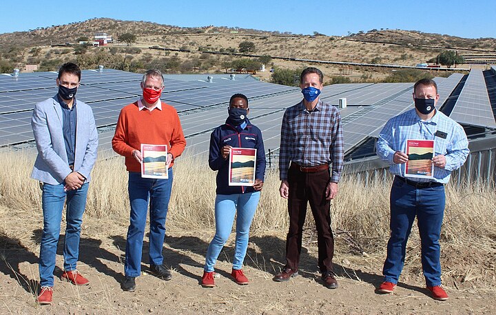 Bild von Personen, die vor Sonnenkollektoren stehen, die den Bank Windhoek Green Bond Impact Report halten