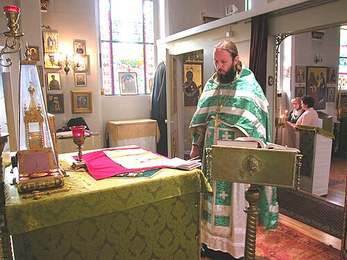 A Russian Orthodox priest celebrating Divine Liturgy. On the Holy Table (altar) is a green indítia, and the Antimens (gold) with its eileton (red) has been opened.