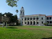 Um imponente prédio antigo da escola com uma torre do relógio, visto em um grande gramado verde