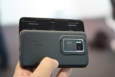 The 5-megapixel camera on the back of the Nokia N900. The hatch is open. The tilt stand is seen surrounding the camera.