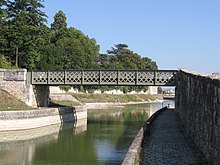 Photo couleurs. Passerelle franchissant le canal sur le bief de Saint-Jean-de-Braye. Il s’agit d’un pont en poutre droite en treillis, peint en gris.