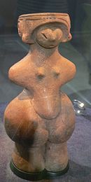 Photo couleur d'un présentoir sous vitre d'un musée, sur lequel se tient unee statuette en terre cuite de couleur ocre représentant une femme enceinte.