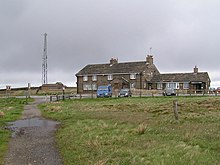 Inn building behind vehicles in car park, with nearby mobile phone tower to rear