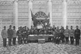 Verklaring van die Jung Turke Revolusie in 1908 deur die leiers van die Ottomaanse millets, met ’n paar Ottomaanse vlae.