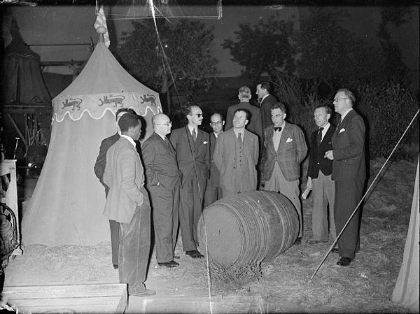 1942: Overseas newspaper correspondents inspect a beer barrel and tent 'at Agincourt', part of the set built for the production of 'Henry V' at Denham