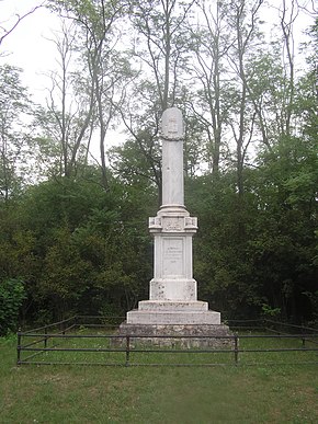 Coluna memorial branca, cercada por uma cerca baixa