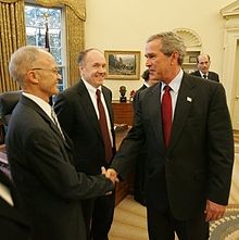 Bush le da la mano a Kydland con Prescott detrás de ellos.