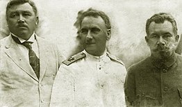 Photographie en noir et blanc de face de trois hommes ne regardant pas la caméra (sauf celui de droite), avec un à gauche, un au centre et un à droite.