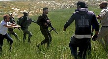 Armed Israeli settler accompanied by soldiers threatens Palestinian farmers near a-Tuwani, South Hebron Hills Settler violence.jpg