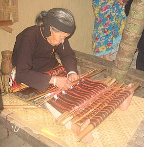 This Hlai weaver tensions her traditional backstrap loom with her feet. Hainan Island, Southern People's Republic of China.