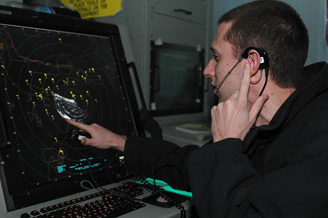 Naval air traffic controller communicates with aircraft over a two-way radio headset