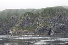 Falaise rocheuse en bord de mer, avec un ciel gris.