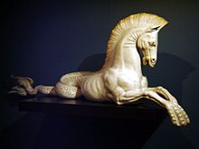 sculpture blanche d’une créature mi-cheval mi-poisson présentée de profil, sa queue enroulée à l’arrière et ses antérieurs étant palmés.