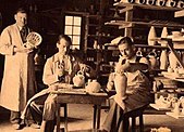 Fotografía en blanco y negro del interior de un taller con tres personas trabajando.