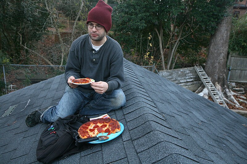 File:Man eating pepperoni pizza on a roof.jpg