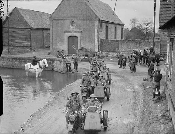 Motorcycle combinations of the 4th Battalion, Royal Northumberland Fusiliers pass through a village, watched by the local inhabitants, France, 20 Marc