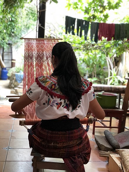 An indigenous woman of the Maya Tzutujil culture weaves using a back-strap loom.