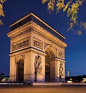 Seitliche Nachtaufnahme eines Triumphbogens mit Lichtspuren im Vordergrund und dem Eiffelturm im rechten Hintergrund. Zwei Torbögen führen ins Innere und im oberen Bereich sind drei Szenenreliefs zu sehen. Unter dem Dachgesims befindet sich ein Szenenrelief, das über alle Seiten geht.