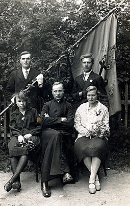 Board members a group in Darbenai with a local priest and Pavasaris flag Board of Pavasaris group in Darbenai.jpeg