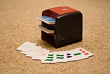 A small, modern tabletop shuffling machine, used on a deck of Set cards Card shuffler with Set cards.jpg