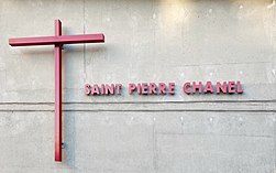 Croix rouge et inscription "Saint Pierre Chanel" en rouge, sur un mur en béton.