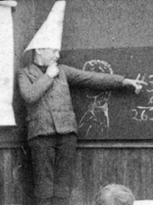 A young boy wearing a dunce cap in class, from a staged photo c. 1906 Dunce cap from LOC 3c04163u.png