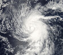 A photograph of a tropical storm over the Eastern Pacific Ocean. It has a tight and well-organized cloud pattern; near the center is a small area of blossoming convection to the right of a tiny hole in the cloud cover.