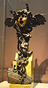 Beeldhouwwerk.  Masker van Medusa, mond wijd open, met vleugels in haar haar evenals gedraaide hagedissen en slangen die als haar kousen dienen.
