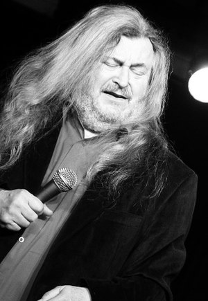 František Ringo Čech close-up, holding a microphone onstage with eyes closed