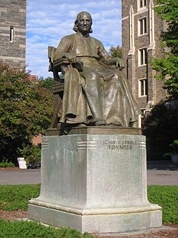Photograph of the statue with a blue sky and stone buildings in the background