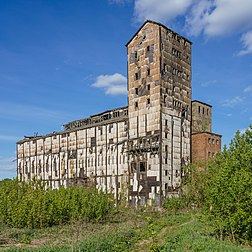 Elevador de grãos abandonado em Falyonki, região de Kirov, Rússia. Um elevador de grãos é um complexo de instalações agrícolas projetado para estocar ou armazenar grãos. No comércio de grãos, o termo “elevador de grãos” também descreve uma torre contendo um elevador de caçambas ou um transportador pneumático, que recolhe grãos de um nível inferior e os deposita em um silo ou outra instalação de armazenamento. Antes do advento do elevador de grãos, os grãos eram geralmente manuseados em sacos e não a granel (grandes quantidades de grãos soltos). Os primeiros elevadores de grãos e silos eram frequentemente construídos de madeira emoldurada ou crivada e eram propensos a incêndios. Caixas de elevadores de grãos, tanques e silos agora são geralmente feitos de aço ou concreto armado. (definição 4 812 × 4 812)