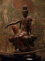 En træudskæring af en siddende buddhistisk figur i løstsiddende, malede gevandter.