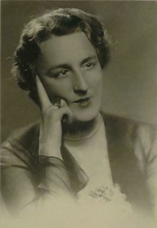 Černobílá fotografie ženy středního věku s krátkými vlasy s pravou rukou položenou na tváři.