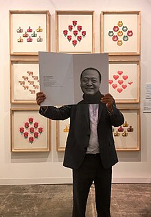 Nan Qi houdt een catalogus omhoog met hemzelf op zijn stand op Art Basel Hong Kong 2017