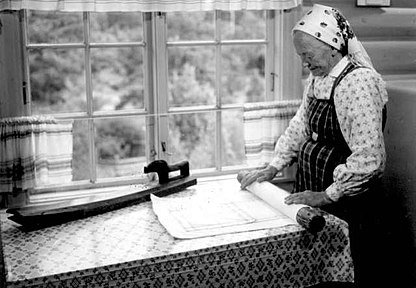 Vanem naine akna all laua peal tekstiili ümber vaalikaika rulli keeramas, laual on ka ka käepidemega vaalikurikas