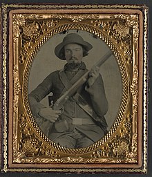 Soldaat Elijah S. Leach, B Company, 31st Virginia Infantry, in uniform, met musket, doos met primers en tas.