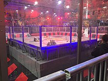 The Robot Wars arena, as pictured for the filming of Robot Wars Series 10 in 2017. Bots pictured are Behemoth (a scoop flipper), Donald Thump (a vertical bar spinner), Sabretooth (a drum spinner), and house robot Shunt (a non-competitor with a lifting scoop and bladed axe). Robot Wars Arena.jpg