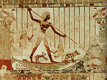 Photo of painting displaying man standing on boat with two small dogs, pointing spear at fish