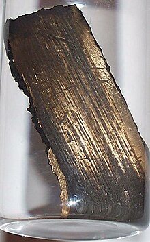 Smećkasta metalna cjepanica nalikuje na komad drveta, s linijama koje se pružaju cjelom dužinom.