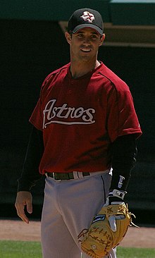 A baseball player standing at first base with his glove, wearing a red jersey with the word 