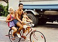 Uma família de três pessoas repartindo uma bicicleta, 1994.